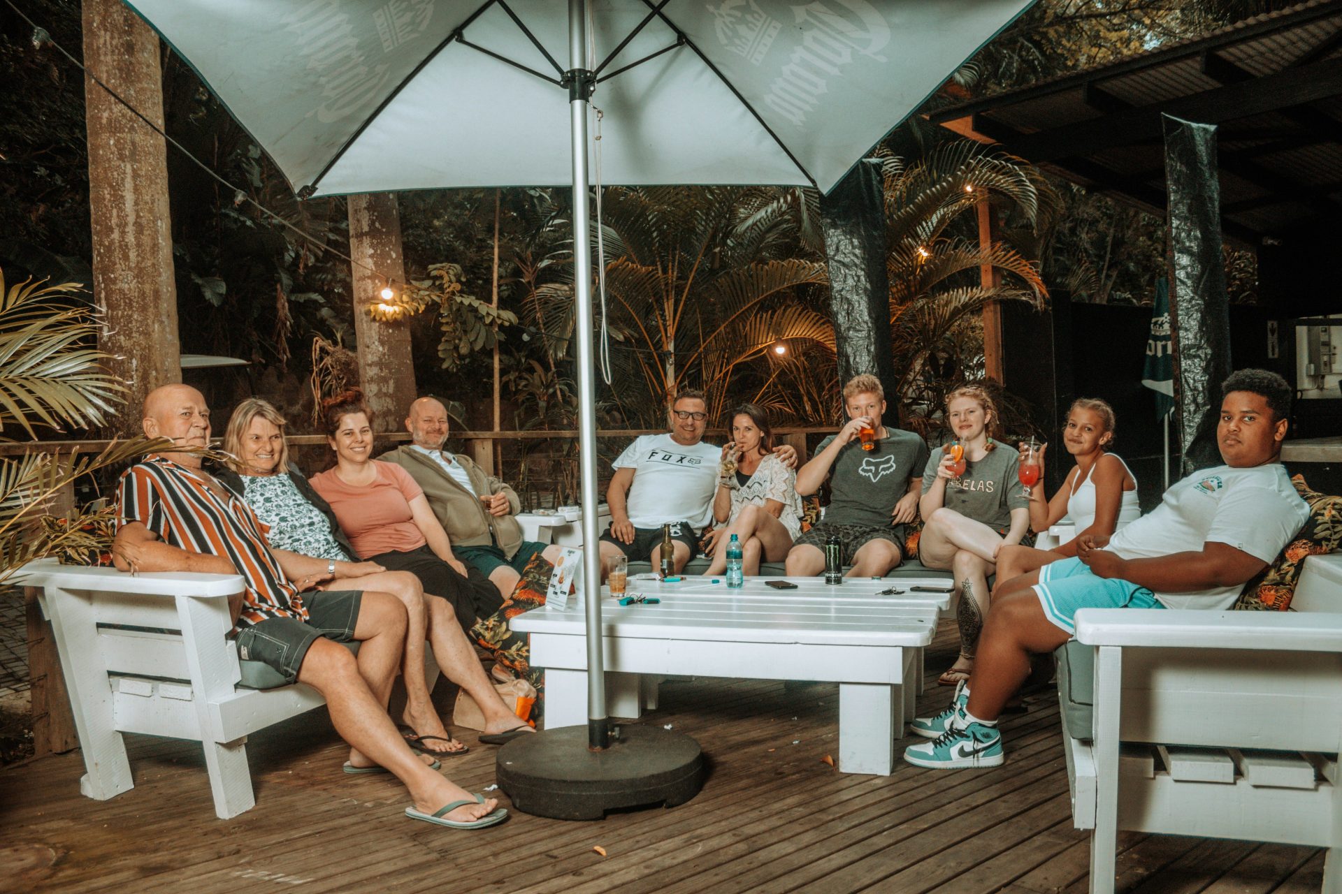 a group of people sitting on white chairs under an umbrella